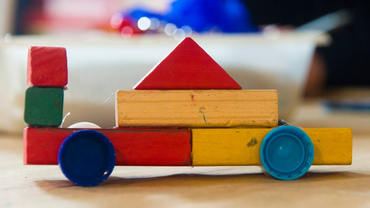 Brinquedo de criança de madeira. São pequenas peças coloridas (vermelhas, verde, azul e amarelo) que montadas formam um carrinho