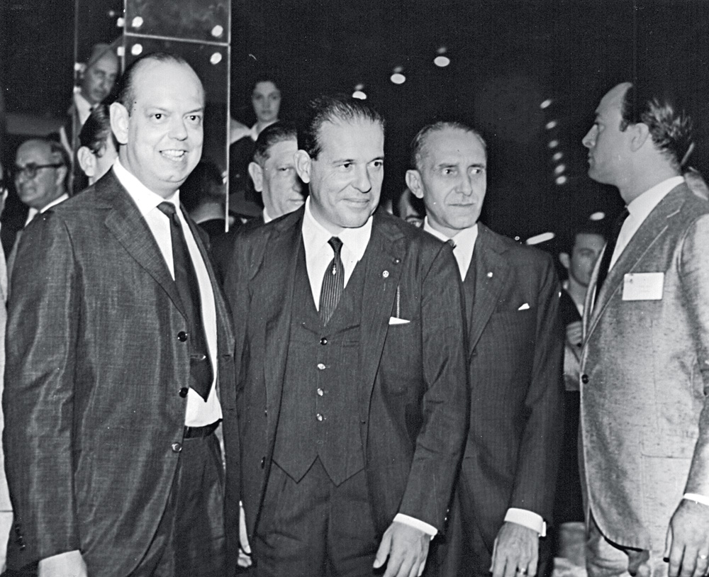 CAM Pres Joao Goulart Min Carvalho Pinto Paulo Passos.jpg A imagem em preto e branco exibe três homens juntos, de pé, sem olharem diretamente para a câmera. Todos vestem ternos. A partir da esquerda, aparecem Caio de Alcântara, o presidente João Goulart e o então ministro da Fazenda, Carvalho Pinto.
