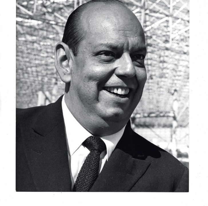 A imagem é um retrato, 3x4, do rosto de Caio. Ele está de terno e sorrindo.