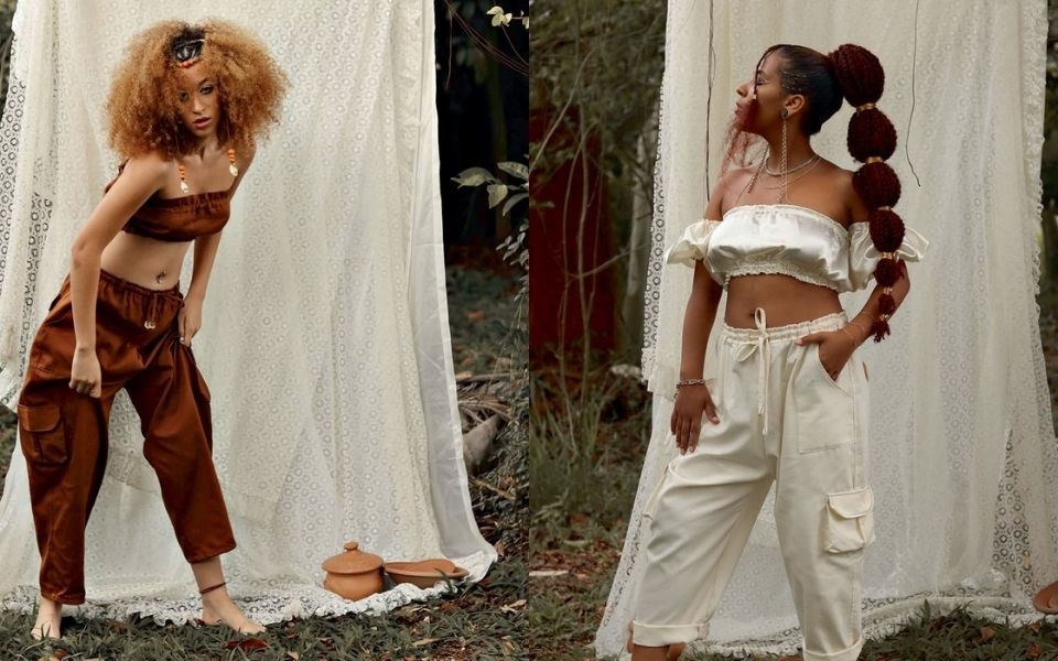 Design sem nome Montagem com menina que posa em frente a um lençol branco estendido. Tem cabelo crespo ruivo e veste um top e uma calça vinho. Outra menina posa em frente a um lençol branco estendido. Tem cabelo crespo vermelho preso e veste top e calça branca
