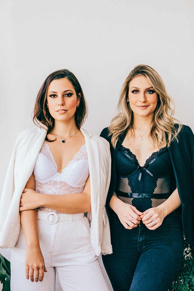 clubes-de-assinaturas-LingeBox.jpg Karol e Karina, da LingeBox, posam para a foto de pé. Karol veste peças brancas e Karina peças pretas, ambas com peças de lingerie inclusas no look.