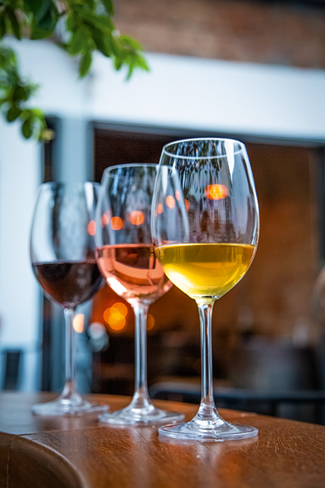 Taças de vinho – Iaiá Cave à Manger Na imagem aparece três taças de vinhos. Uma com tinto, outra com rosé a ultima com vinho branco.