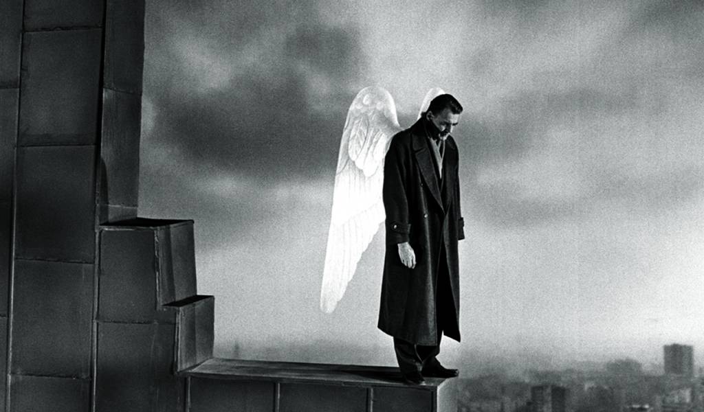 classicosstreaming1 A imagem apresenta um homem no topo de um edifício, na ponta do telhado. Ele tem duas asas de anjo nas costas e a cena aparenta ser melancólica.