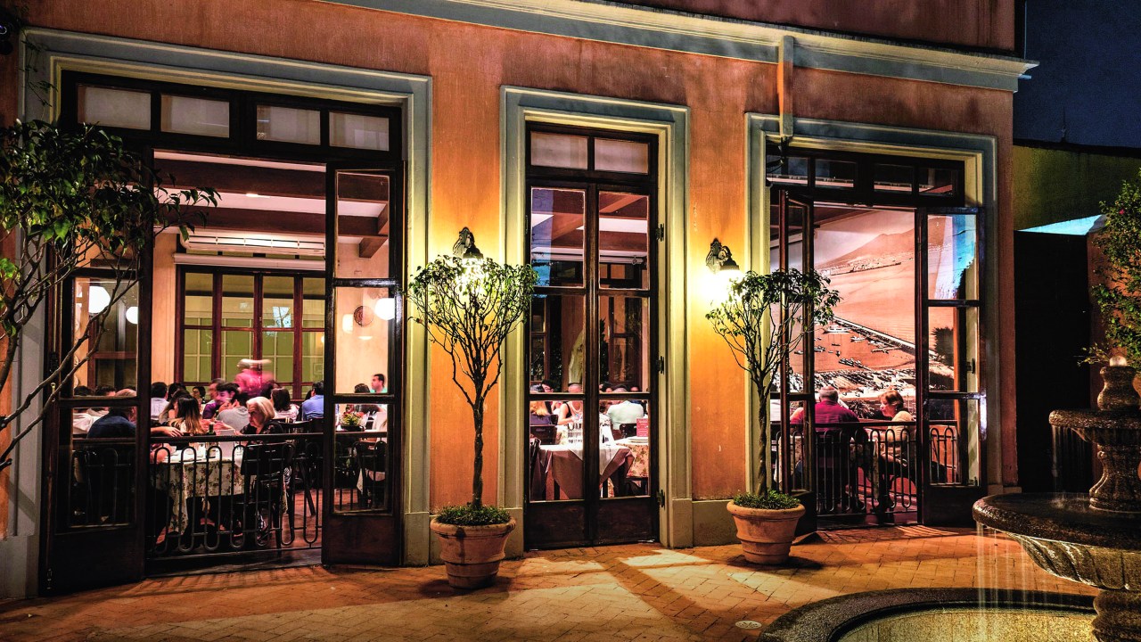 Janelões do jardim interno da pizzaria Speranza, com paredes alaranjadas e pessoas sentadas à mesa na parte de dentro.