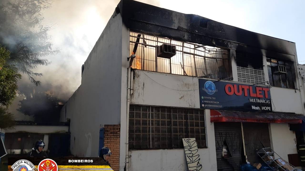 A imagem mostra o galpão destruído pelo fogo. Na fracada está escrito "Outlet multimarcas"