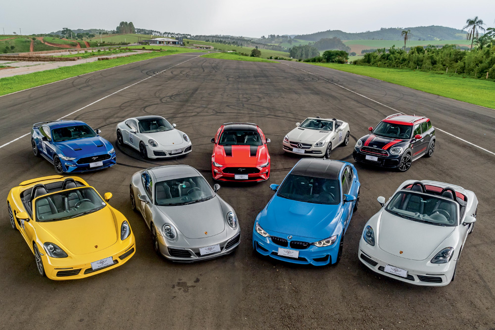Nove carros esportivos de luxo estão estacionados em uma grande pista de corrida