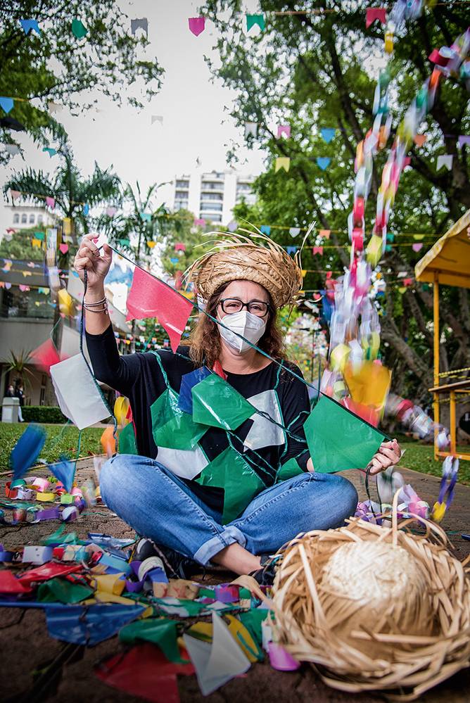 Veja SP Mulher de máscara sentada com pernas cruzadas mostra bandeirinhas coloridas de festa junina