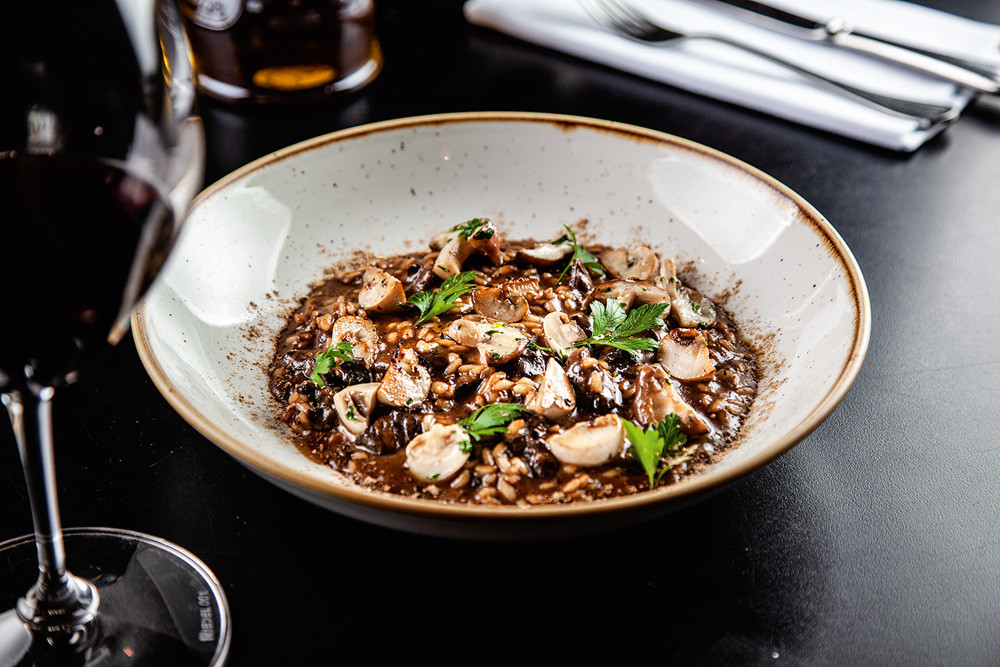 Risoto de cogumelos – Piccini Cucina Risoto de cogumelos ao lado de taça de vinho.