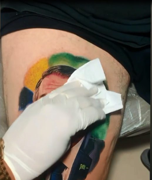 Imagem da mão do tatuador limpando a tatuagem do rosto de Jair Bolsonaro
