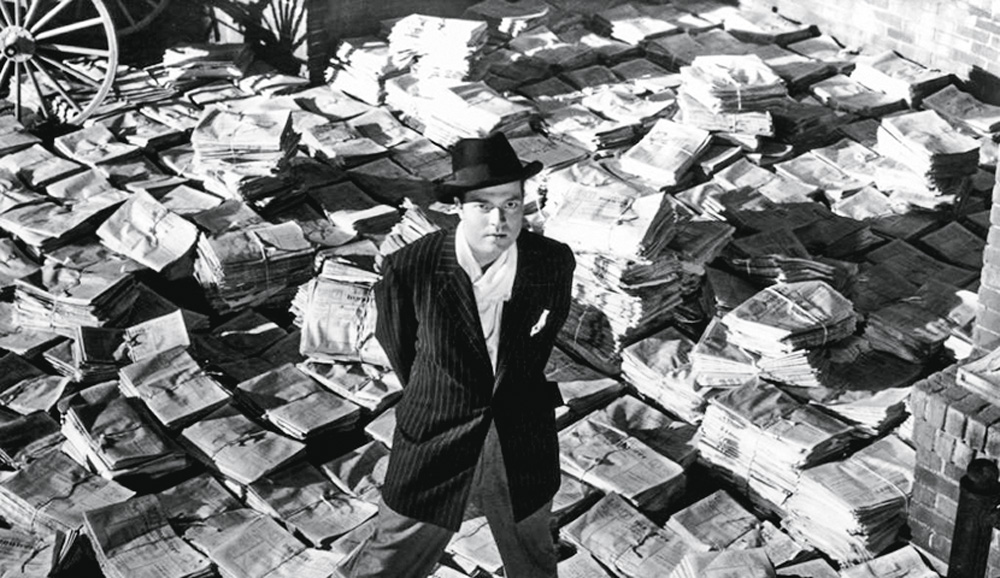 classicos2.jpg A foto mostra o personagem principal do longo sobre uma pilha interminável de jornais