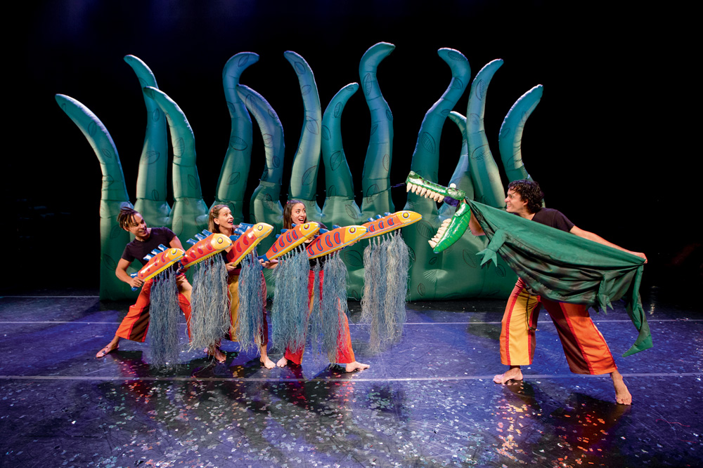 Bichos-do-Brasil-Pia-Fraus-2-Renan-Perobelli-9.jpg Três atores manuseiam bonecos de peixes e outro de um jacaré em um palco de teatro