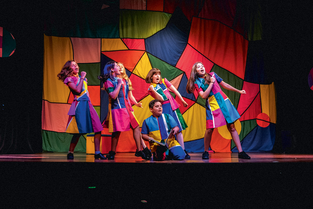Cena de Cade a Crianca… Foto de Adriano Doria XXT32218 (3).jpg Seis crianças em cena, vestidas com a mesma roupa, de formas e coloridas, dançam em um palco de teatro