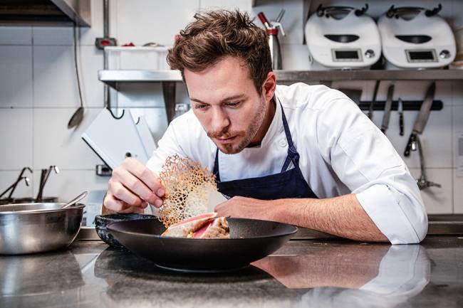 Dalton Rangel finalizando preparo de prato em bancada da cozinha.