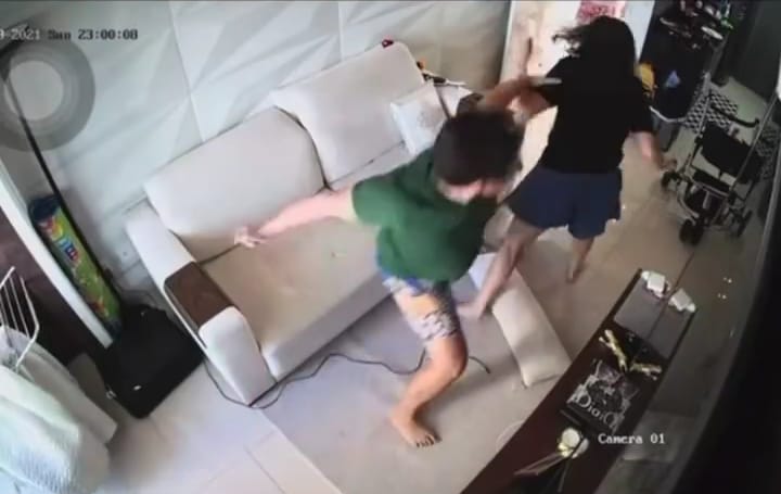 A imagem mostra uma cena congelada da câmera de segurança no momento em que Ivis leva seu braço para trás armando um soco na nuca de Pamela