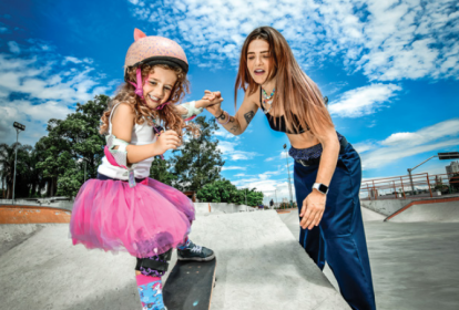 Uma menina equipada com proteção andando de skate de mãos dadas com uma mulher