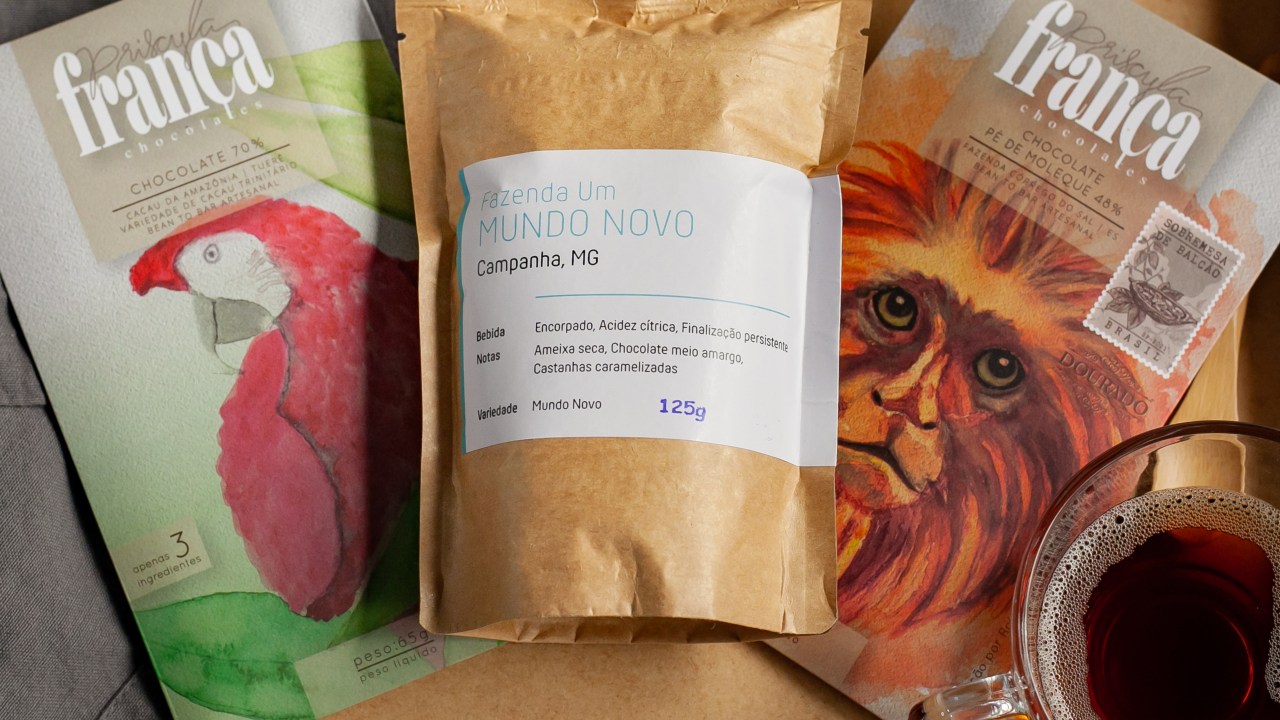 Barras de chocolate da Priscyla França ao com pacote de pardo de café mundo novo da Um Coffee Co. ao centro e xícara de coado no canto direito.