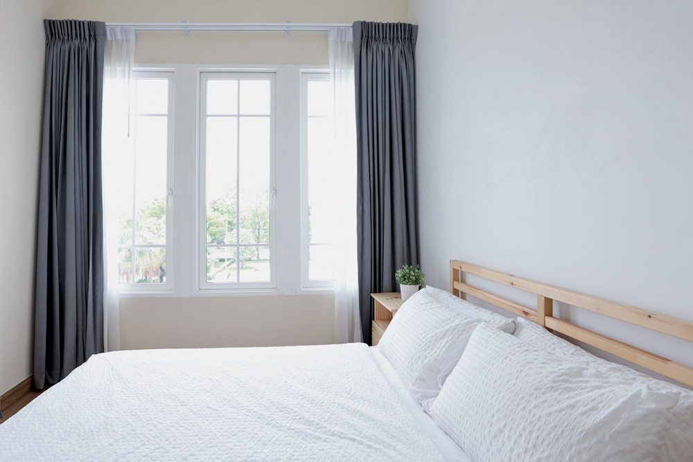 Cama de madeira em frente a janela Vista lateral de uma cama de madeira branca moderna em quarto branco com luz suave e clara