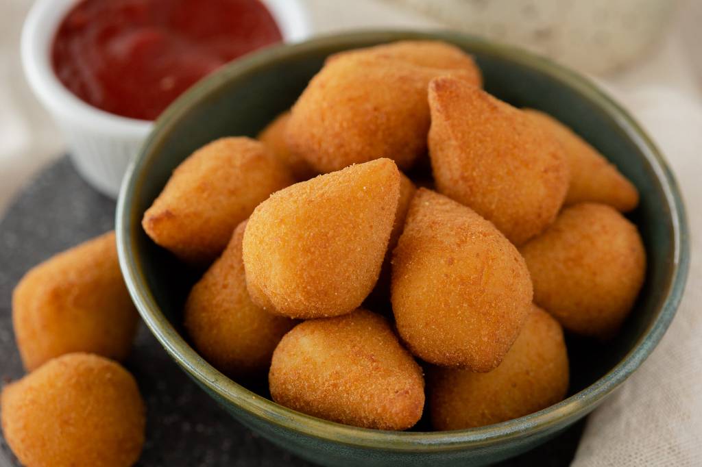 Padaria Real Coxinha Cumbuca com diversas coxinhas pequenas com mais duas à esquerda, fora do recipiente.