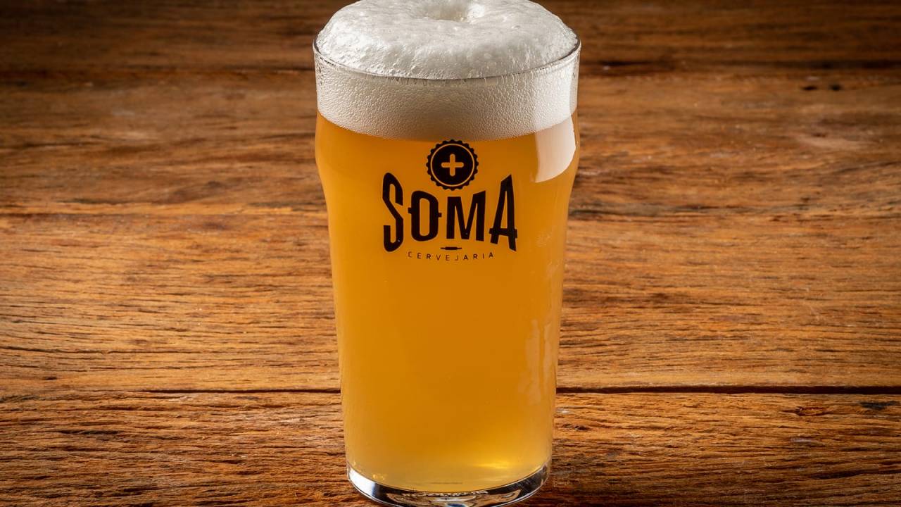 Copo de chope da Soma Cervejaria sobre bancada de madeira.