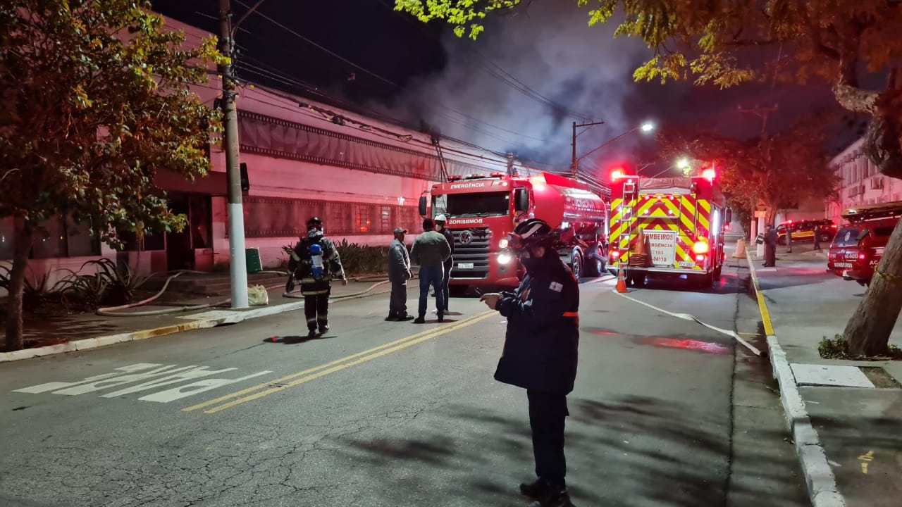 Imagem mostra rua com carros do corpo de bombeiros e edifício, de onde sai fumaça