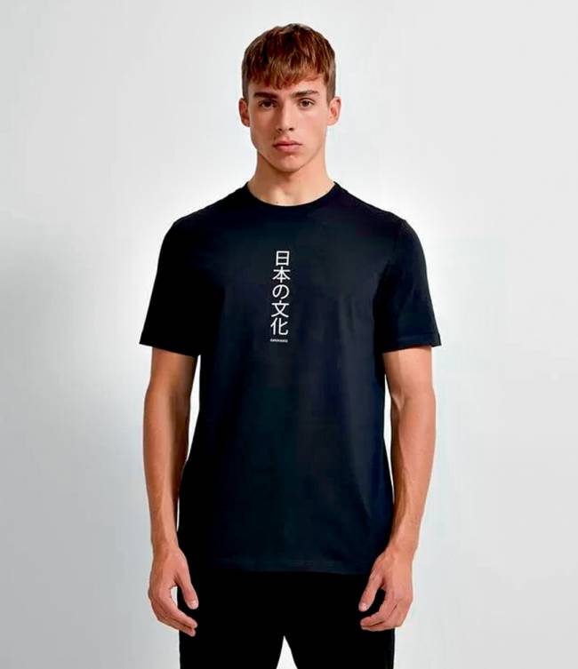 Menino loiro posa para a foto vestindo uma camiseta preta com escrito pequeno em branco em japonês no centro da peça