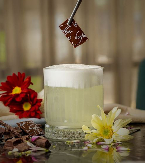 Mocktail Beefbar Drinque claro com espuma branca recebendo pedaço de chocolate com pinça escrito Beefbar.