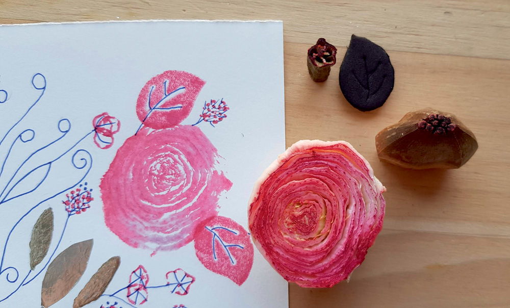 oficina 3161929.jpg Uma folha de papel tem desenhos de folhas e rosas. Uma rosa real está do lado da folha