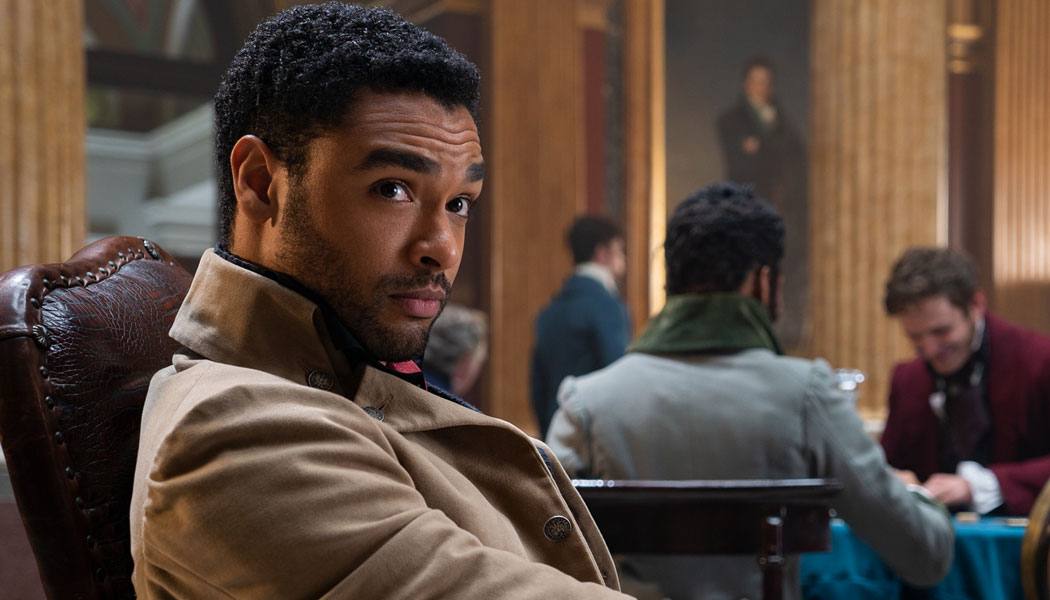 A imagem mostra o ator Regé-Jean Page, na série Bridgerton, olhando de canto para alguém fora da cena