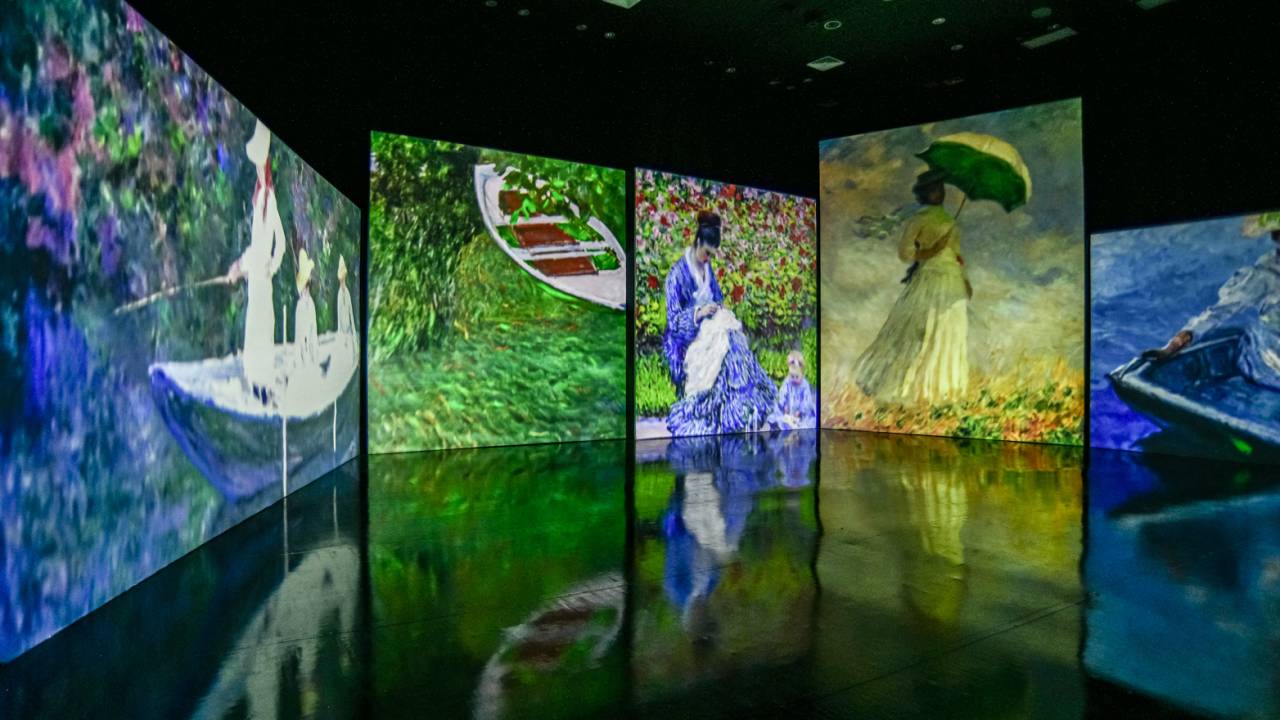 Obras de Monet projetadas na parece em sala de exposição com chão preto.
