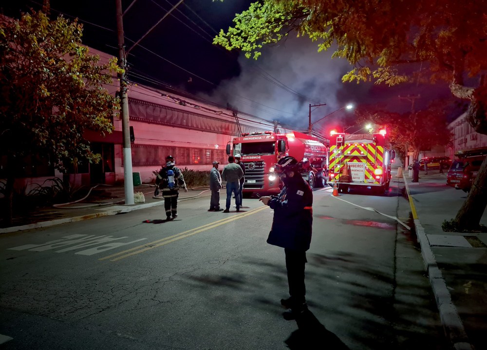 Foto mostra um caminhão do corpo de bombeiros, à noite, com oficiais trabalhando, em frente a um prédio