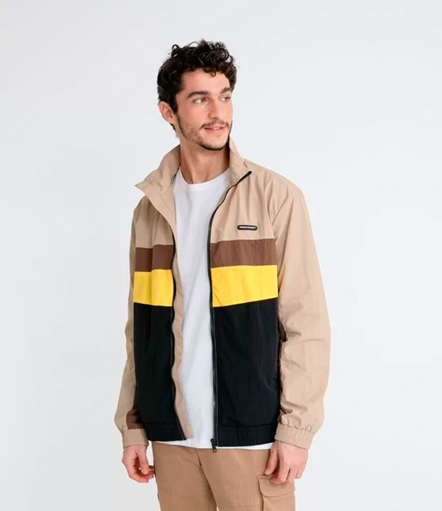 Jaqueta masculina Renner.png Homem veste camisa branca e jaqueta bege com detalhes em amarelo, preto e marrom. Ele olha para o lado