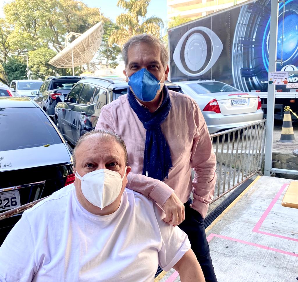 MasterChef Brasil – Erick Jacquin e Arnaldo Lorençato Erick Jaqcuin sentado ao lado de Arnaldo Lorençato na frente dos estúdios da Band. Ambos de máscara.
