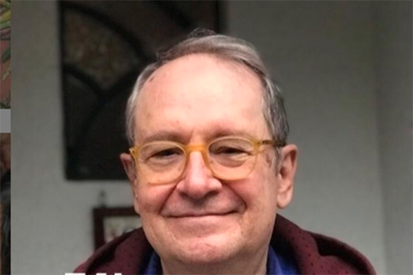 Imagem mostra Zeca sorrindo. Ele usa óculos e casaco