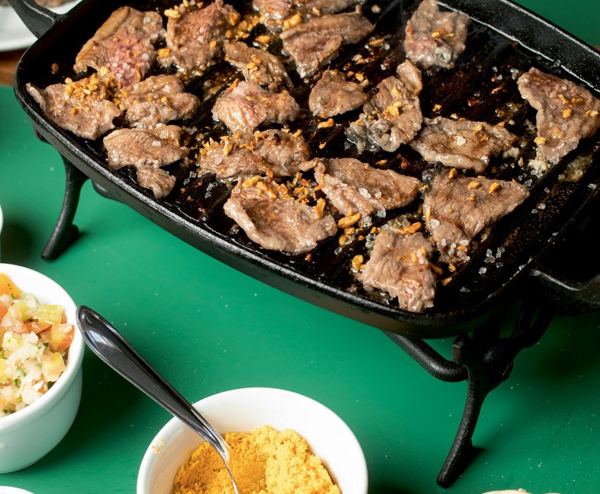 A imagem mostra uma bandeja com pedaços de picanha em cima de uma mesa com o pano verde.