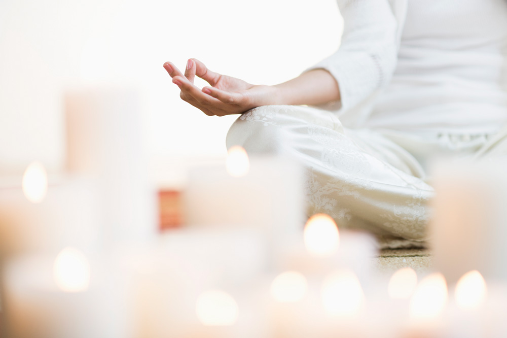 Mulher meditando em posição de lótus perto de velas acesas