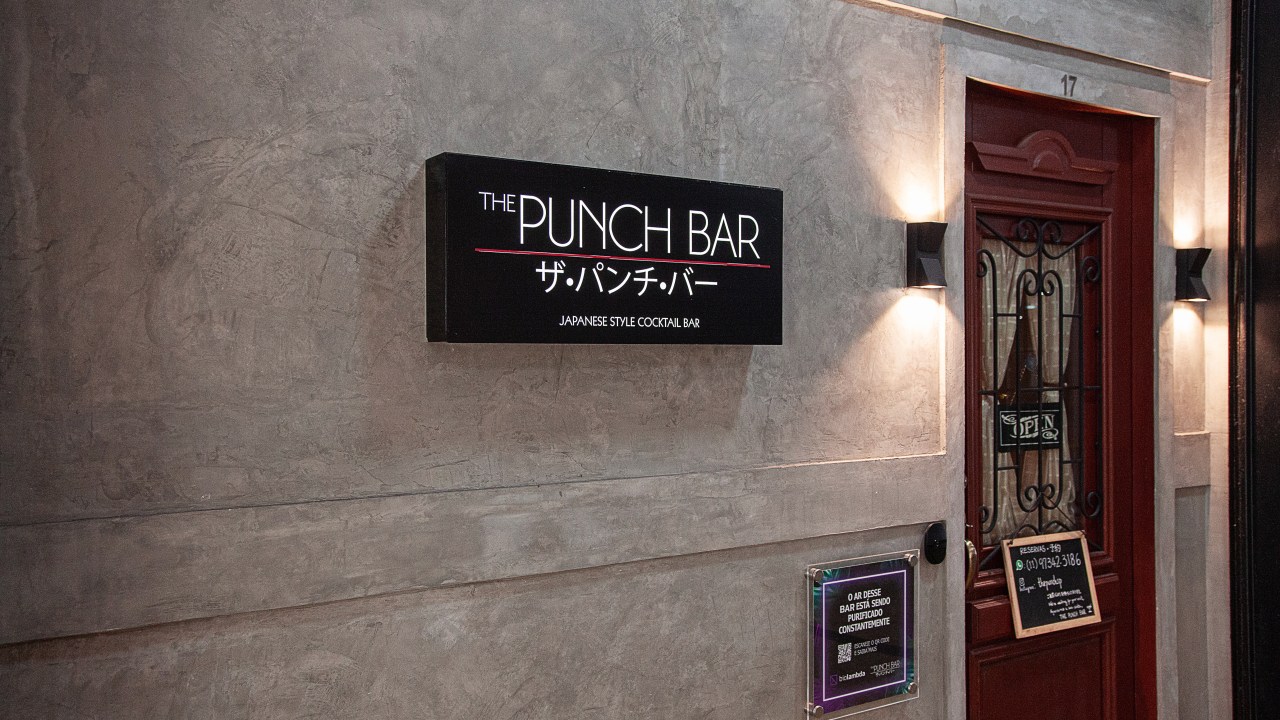 Fachada do The Punch Bar de concreto ao lado da porta de madeira.