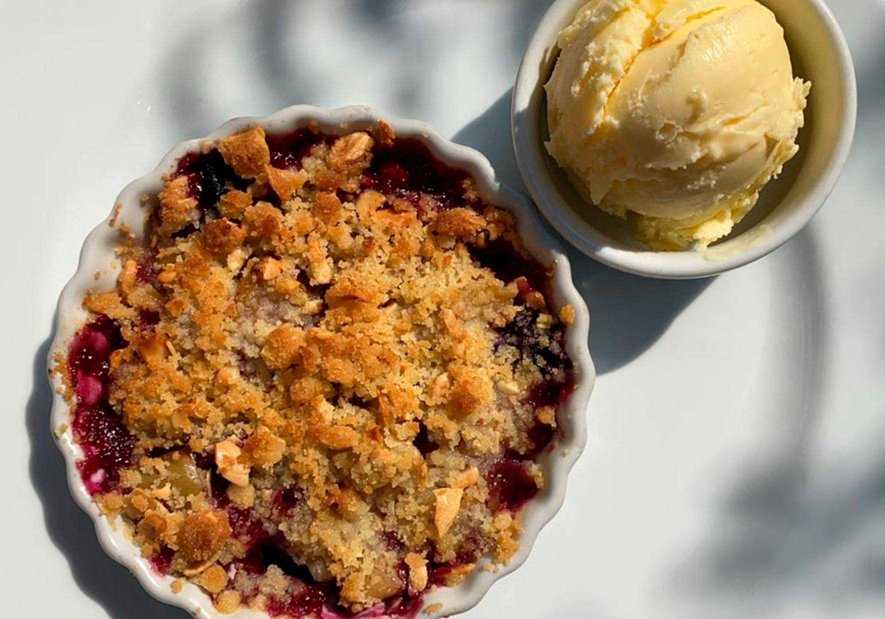 Crumble de ma&ccedil;&atilde; servido em pequena cumbuca de lou&ccedil;a branca ao lado de bola de sorvete de creme.