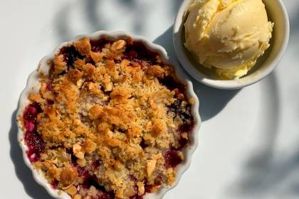 Crumble de ma&ccedil;&atilde; servido em pequena cumbuca de lou&ccedil;a branca ao lado de bola de sorvete de creme.