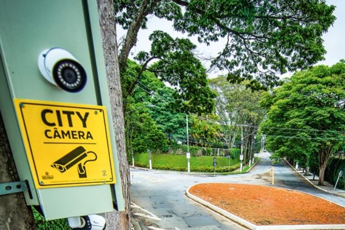 close de câmera de segurança em poste de rua com placa escrito city câmeras embaixo