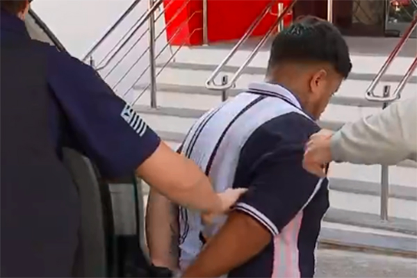 Imagem mostra homem algemado saindo de viatura policial com o auxílio de dois policiais
