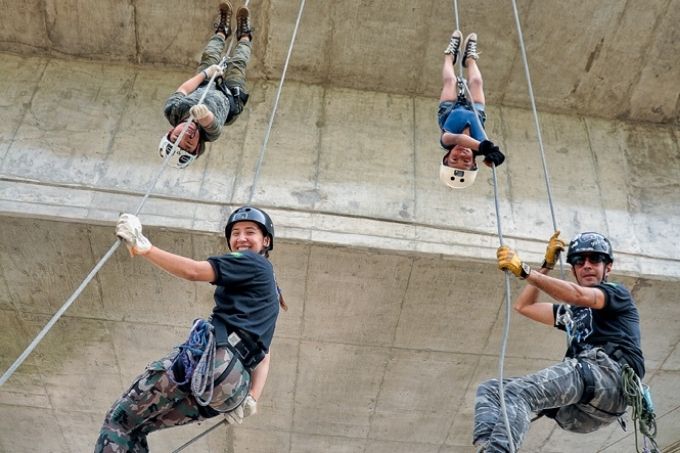 duas crianças e seus respectivos instrutores pendurados realizando rapel de ponte