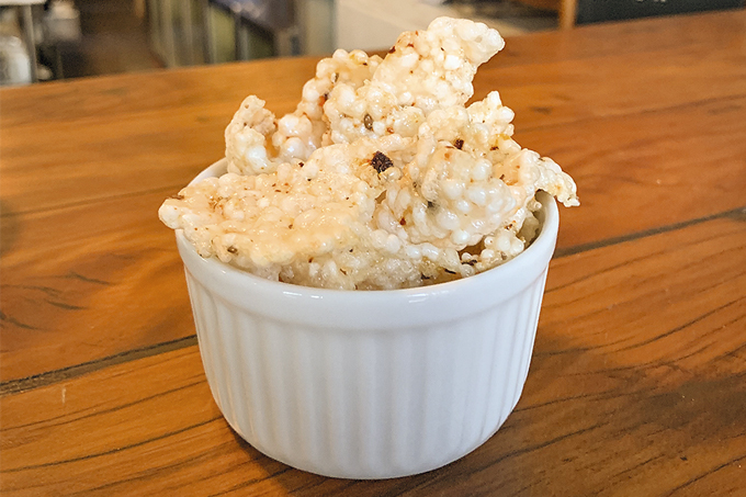 Potinho de louça branca com torresmo de tapioca.