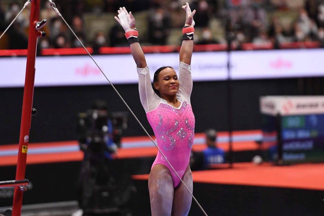 A atleta Rebeca Andrade de braços para cima após terminar apresentação nas barras assimétricas.