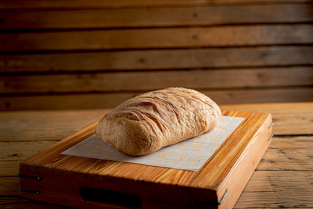 Bagueri Pão do tipo ciabatta fotografado sobre uma tábua de madeira sobre uma mesa