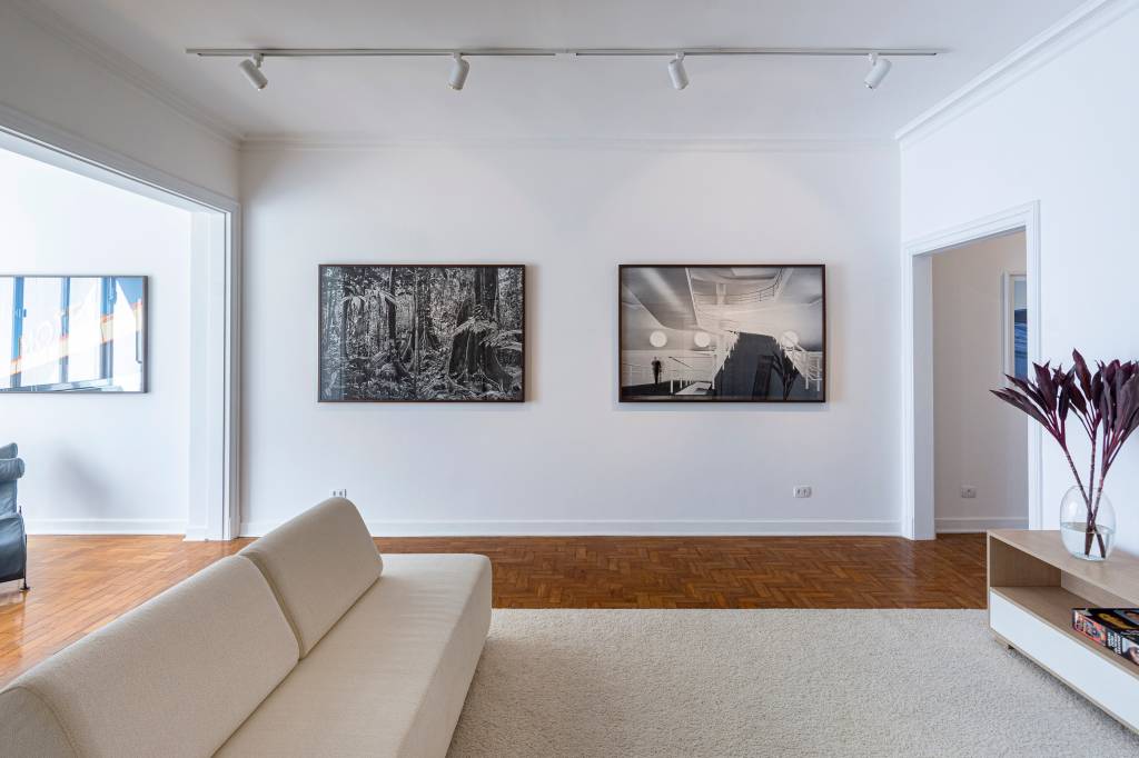 Constance Franciosi – Galeria (DIVULGAÇÃO) (1) Espaço de galeria de Constance Franciosi, inaugurada em prédio dos anos 1940 no Centro, exibe sala com paredes e sofá brancos. Ao fundo, dois quadros exibem fotografias.