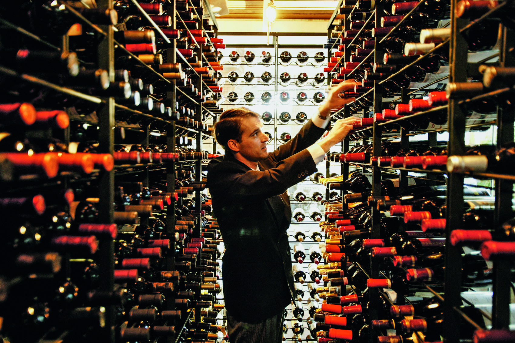 Adega do restaurante A Figueira Rubaiyat com o sommelier escolhendo uma garrafa de vinho ao centro.