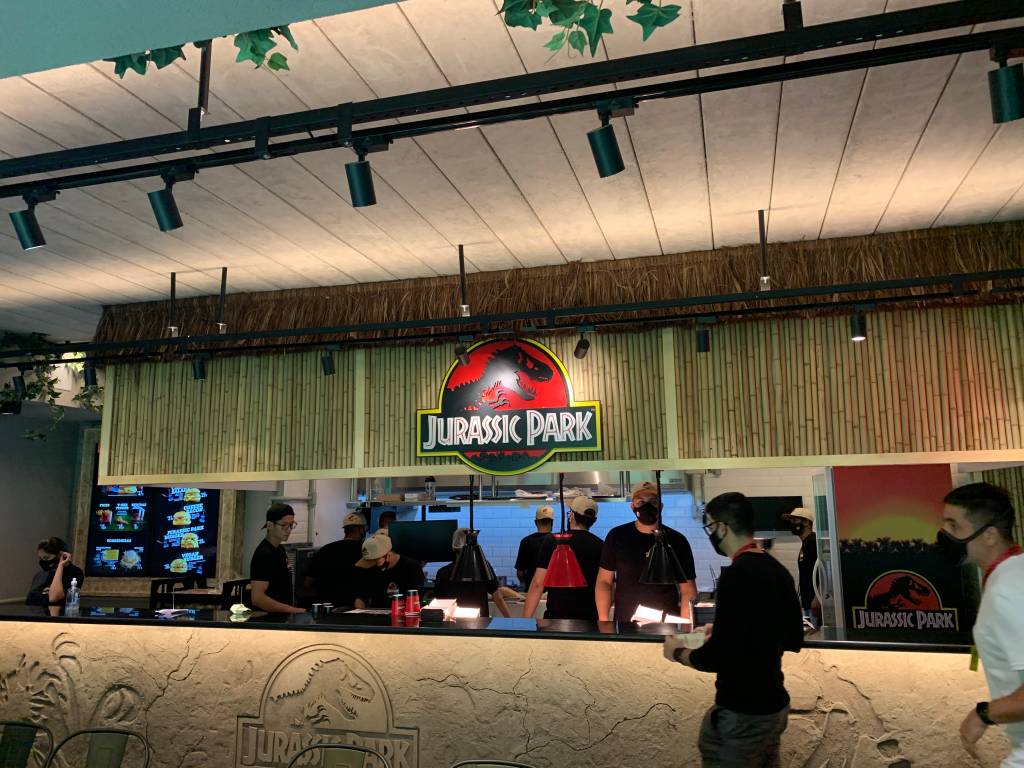 Jurassic Park Burger Restaurant Cozinha da lanchonete Jurassic Park Burger Restaurant aberta para o público. Com balcão de cimento com dinossauro desenhado e teto de bambu.