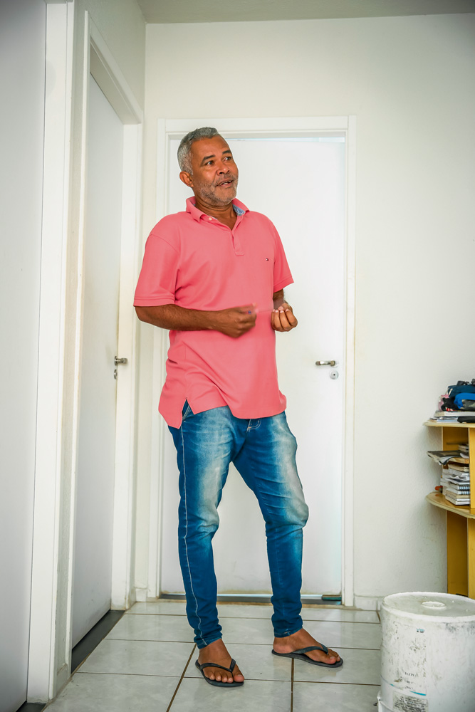 JDAPURA_19.JPG Um homem negro grisalho está gesticulando e conversando em um apartamento branco