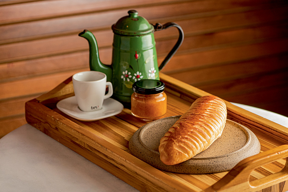 Bagueri Pão fotografado junto de uma xícara, uma chaleira e um recipiente pequeno de vidro sobre uma bandeja de madeira