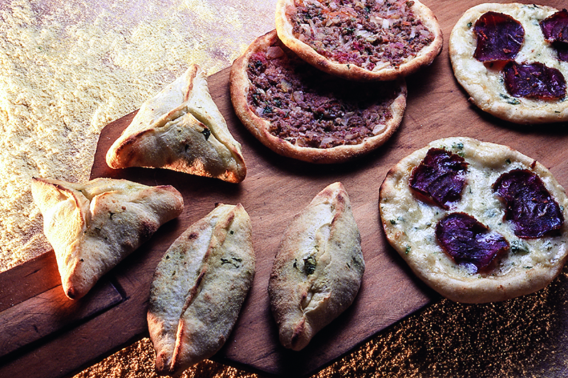 Esfirras abertas e fechadas sobre t&aacute;bua de madeira.